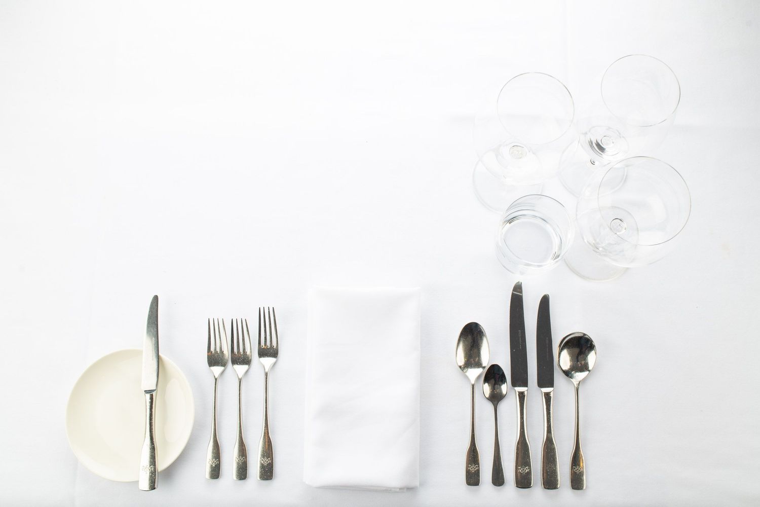 Elegant white table setting with silverware, folded napkin, plate, and crystal glasses.