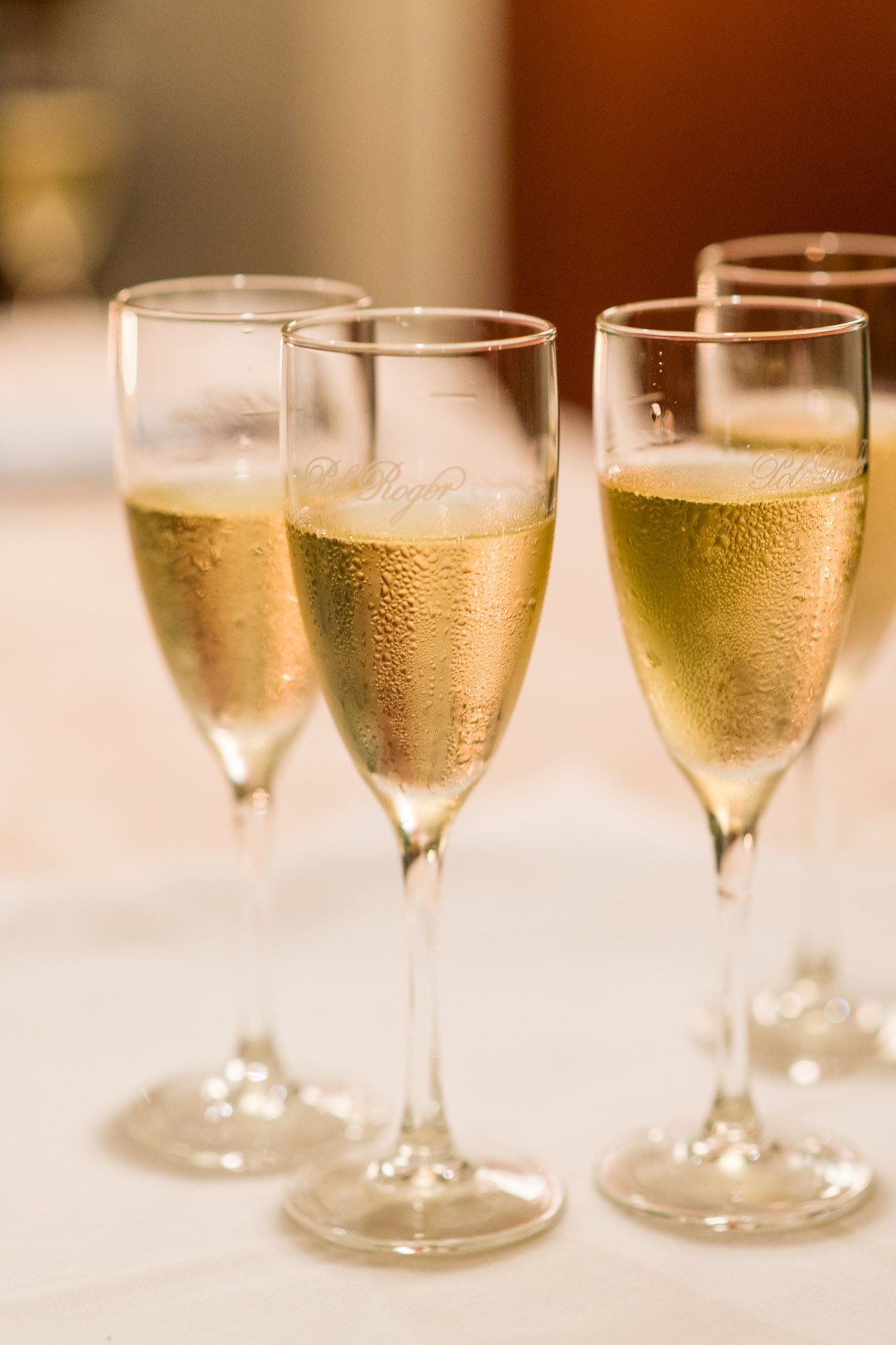 Close-up of four champagne flutes filled with sparkling wine on a white tablecloth at a formal event.