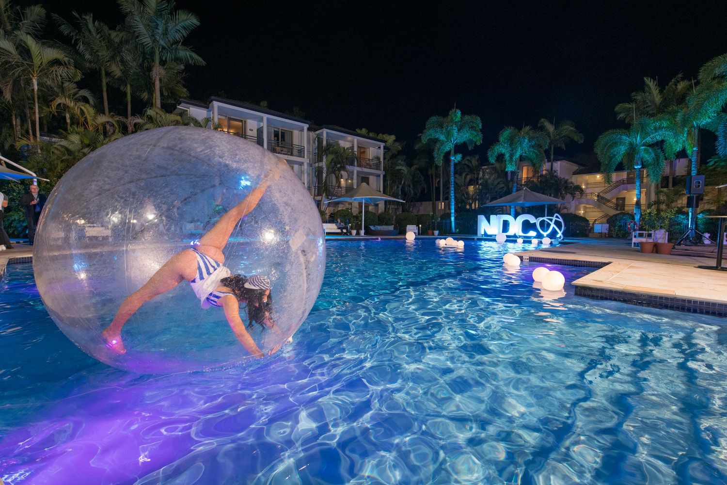 Performer inside transparent water ball floating in illuminated resort pool during spectacular nighttime event.