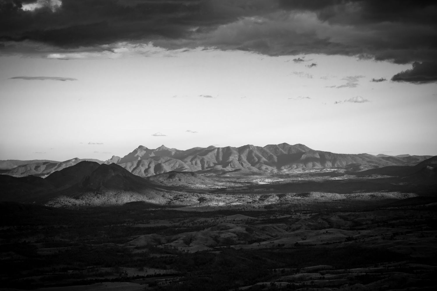 Black and white panoramic landscape of rugged mountain range under dramatic stormy skies in the desert.