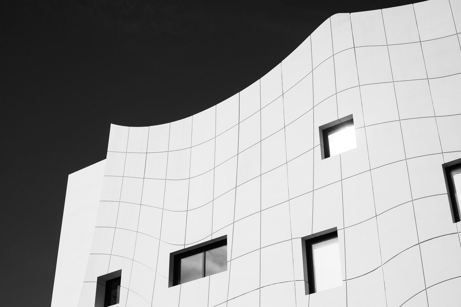 Black and white abstract architecture photo of a curved white tiled building facade with small windows.
