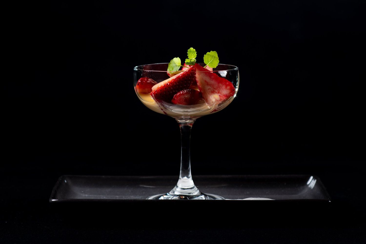 Strawberry dessert in a coupe glass garnished with mint on a dark background.