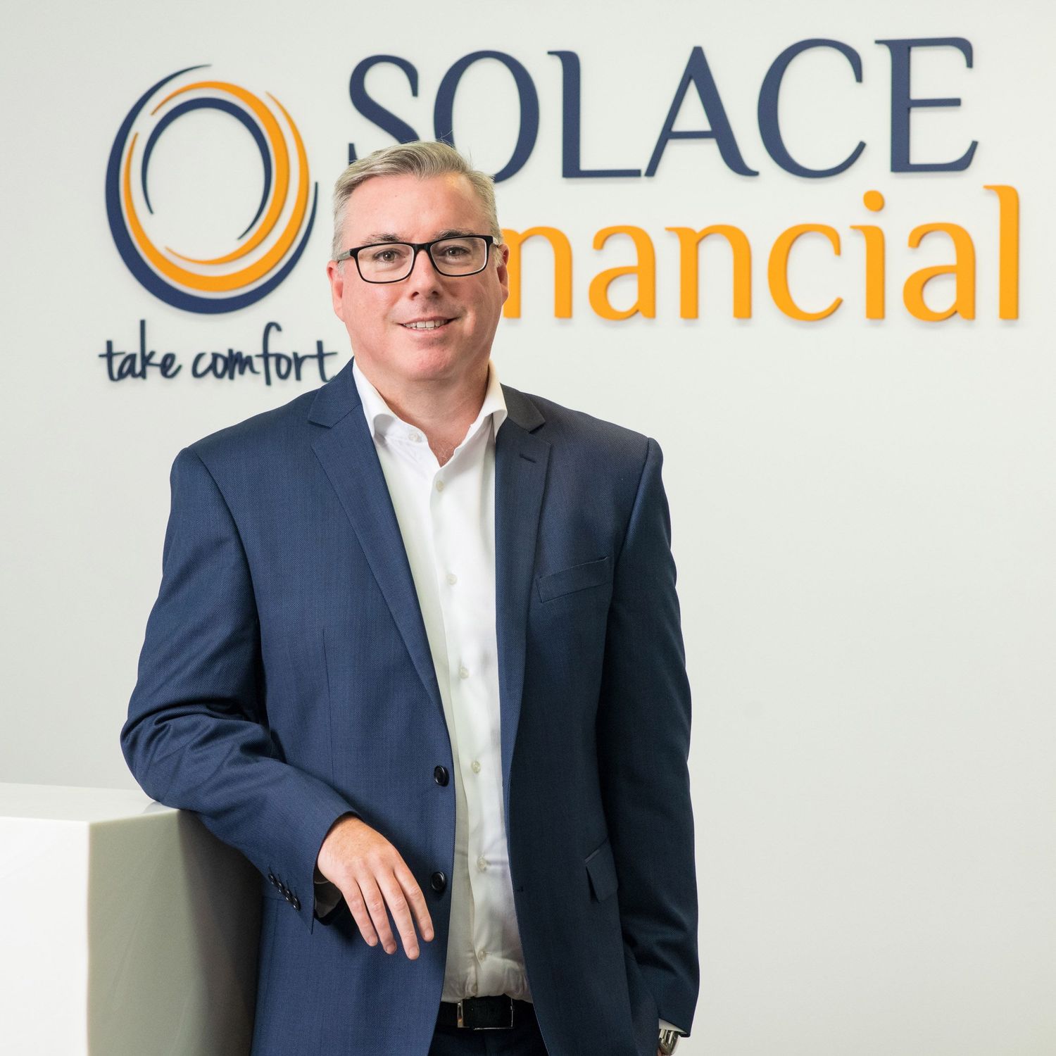 Professional man in blue suit smiling in front of Solace Financial company signage.