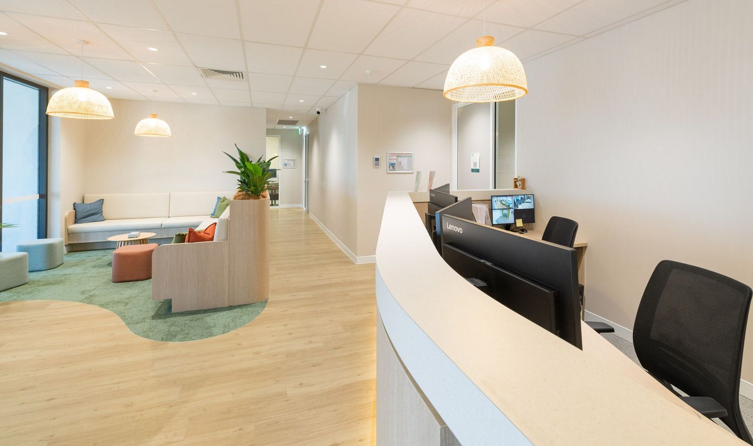 Modern office reception area with white desk, pendant lights, teal carpet, and contemporary Scandinavian-style furniture.