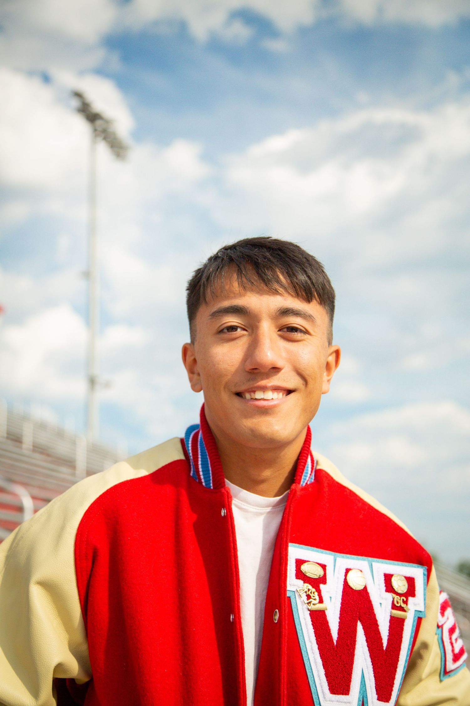 Smiling young man in red and gold varsity letterman jacket at stadium.