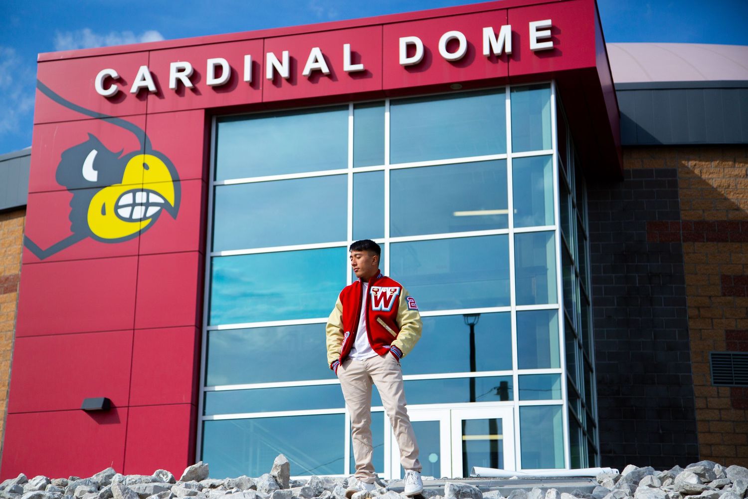Student in varsity jacket standing proudly outside Cardinal Dome entrance.