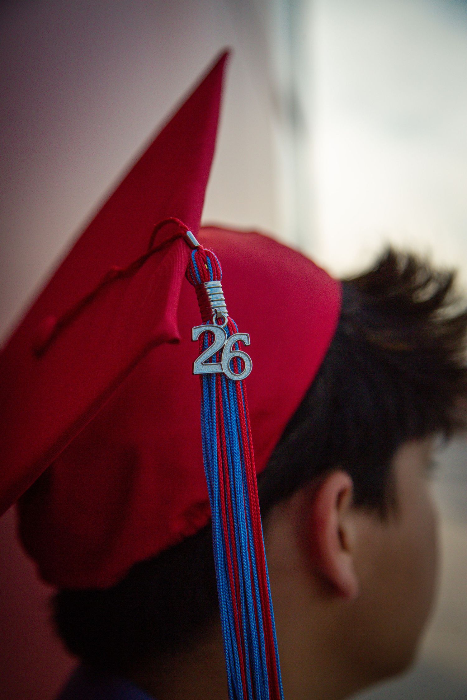 Close-up of a red graduation cap with a blue tassel featuring a silver 26 charm.