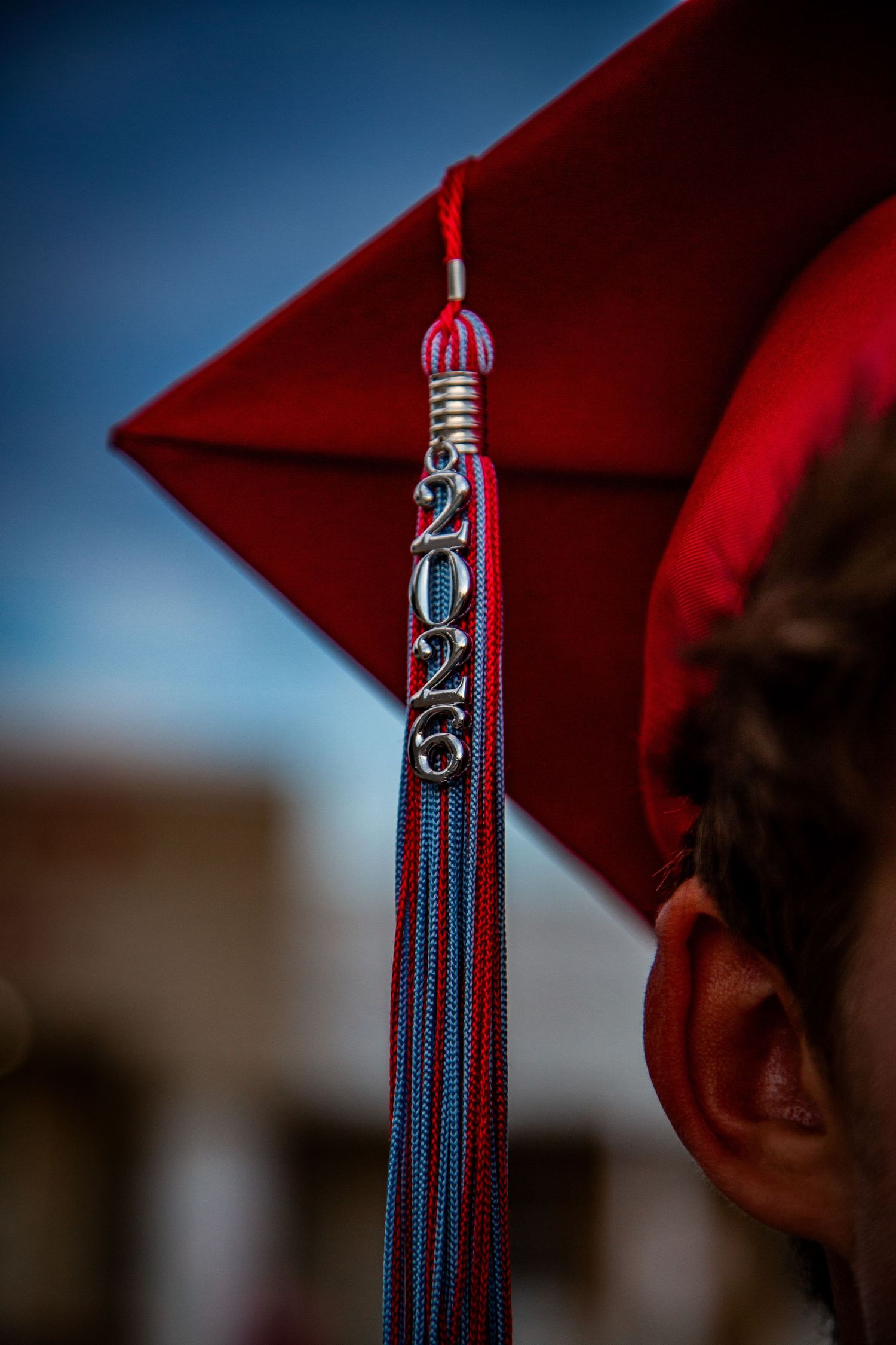 Close-up of a red graduation cap tassel with 2023 charm against a blue sky.