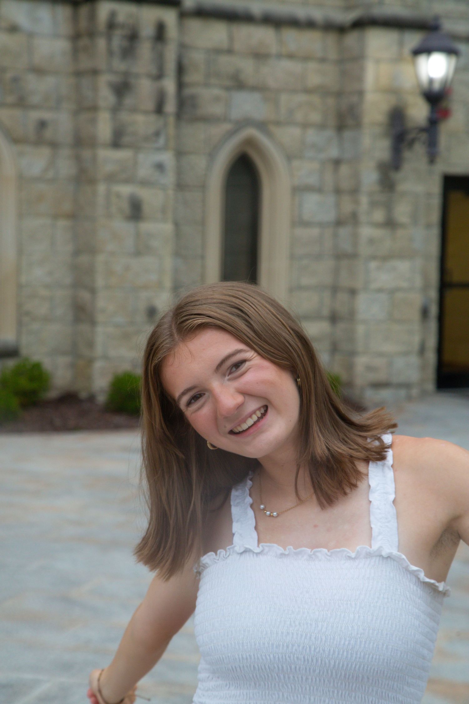 A smiling teenage girl in a white top poses in front of a stone castle building.