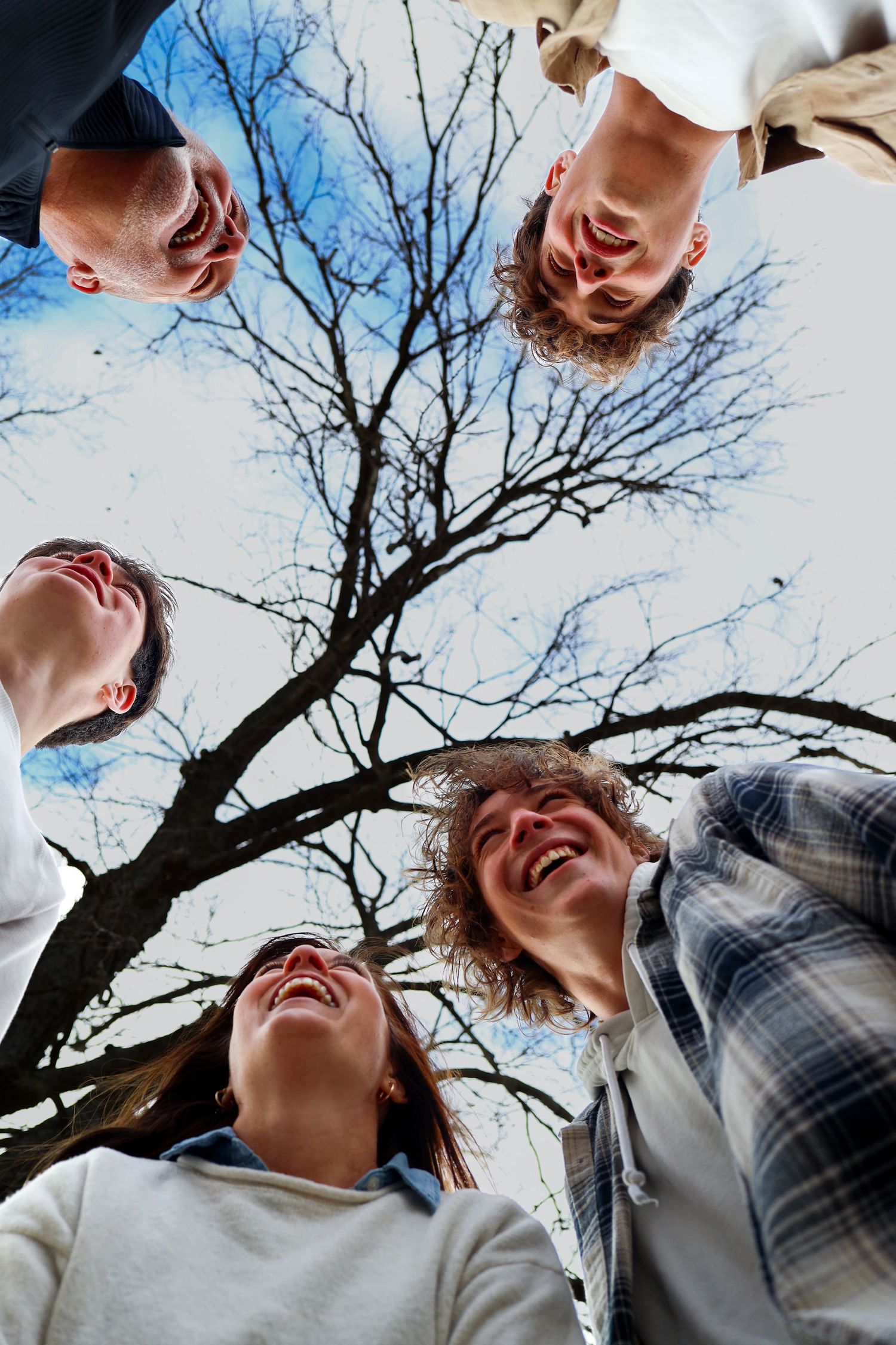 Low angle view of four laughing teens forming a circle under a bare tree.