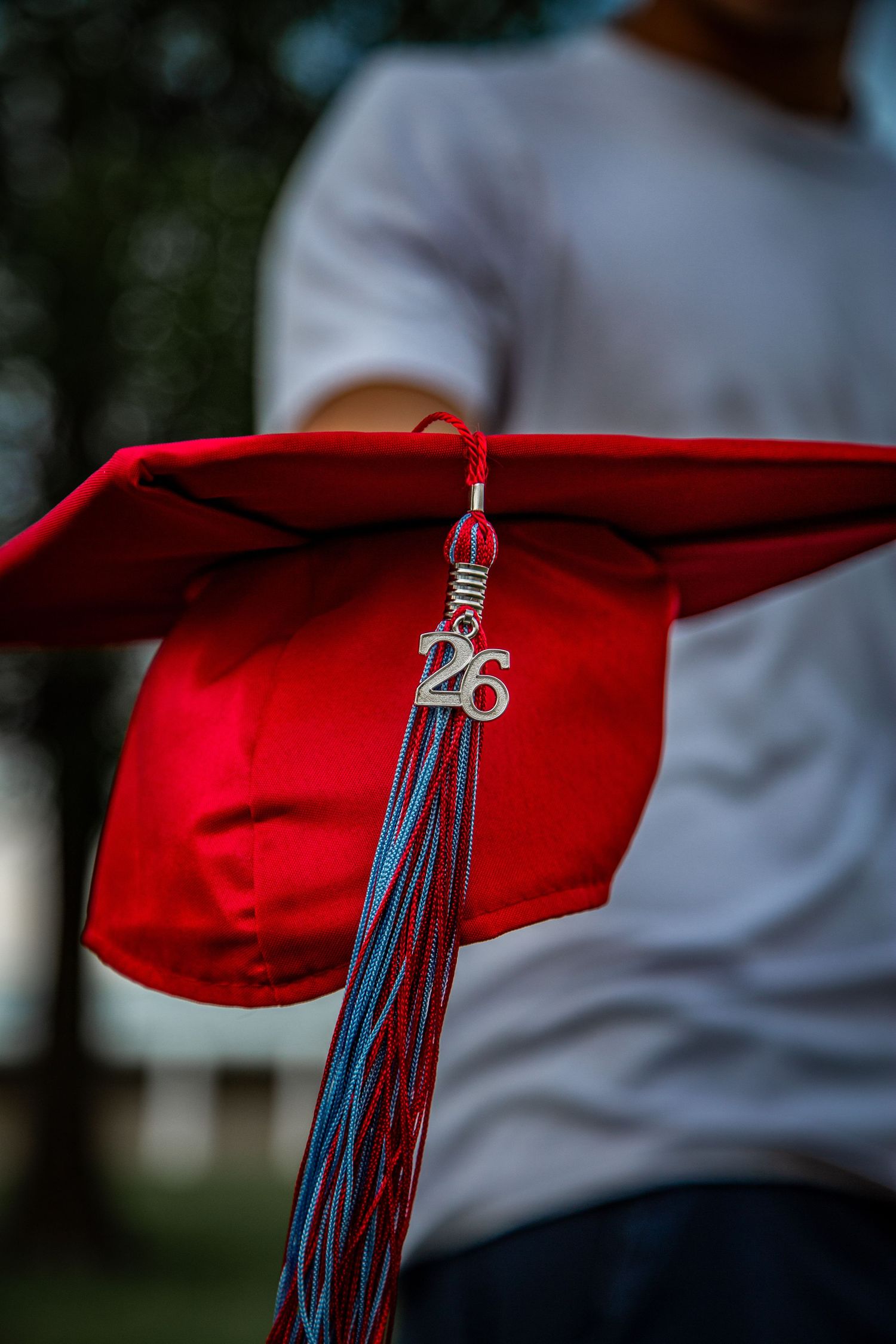 Close-up of red graduation cap with class of 26 tassel charm held by student.