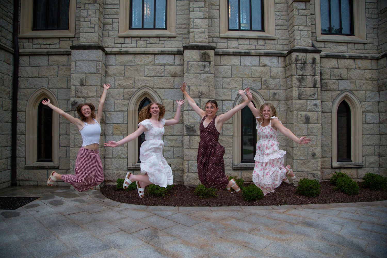 Four girls jumping joyfully in front of a gothic stone church building.