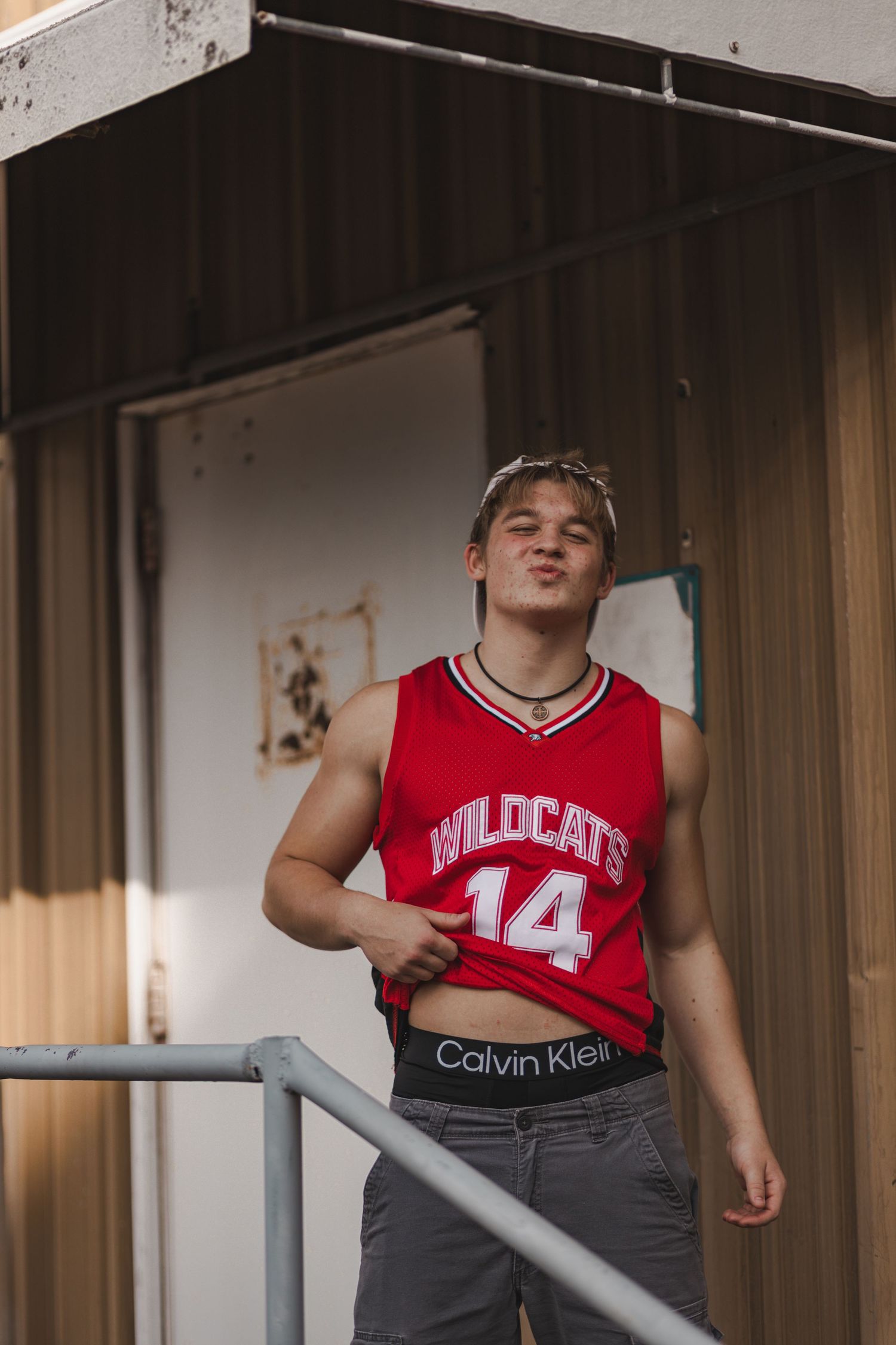 Young man in red Wildcats 14 jersey and Calvin Klein waistband poses on outdoor stairs.
