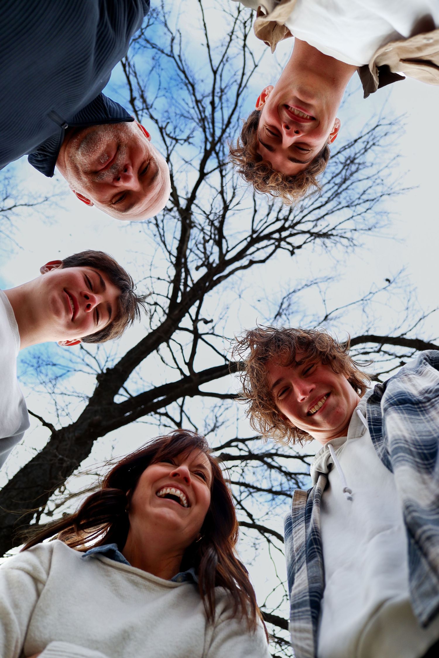 Low angle view of four smiling teens huddled together under a bare winter tree.