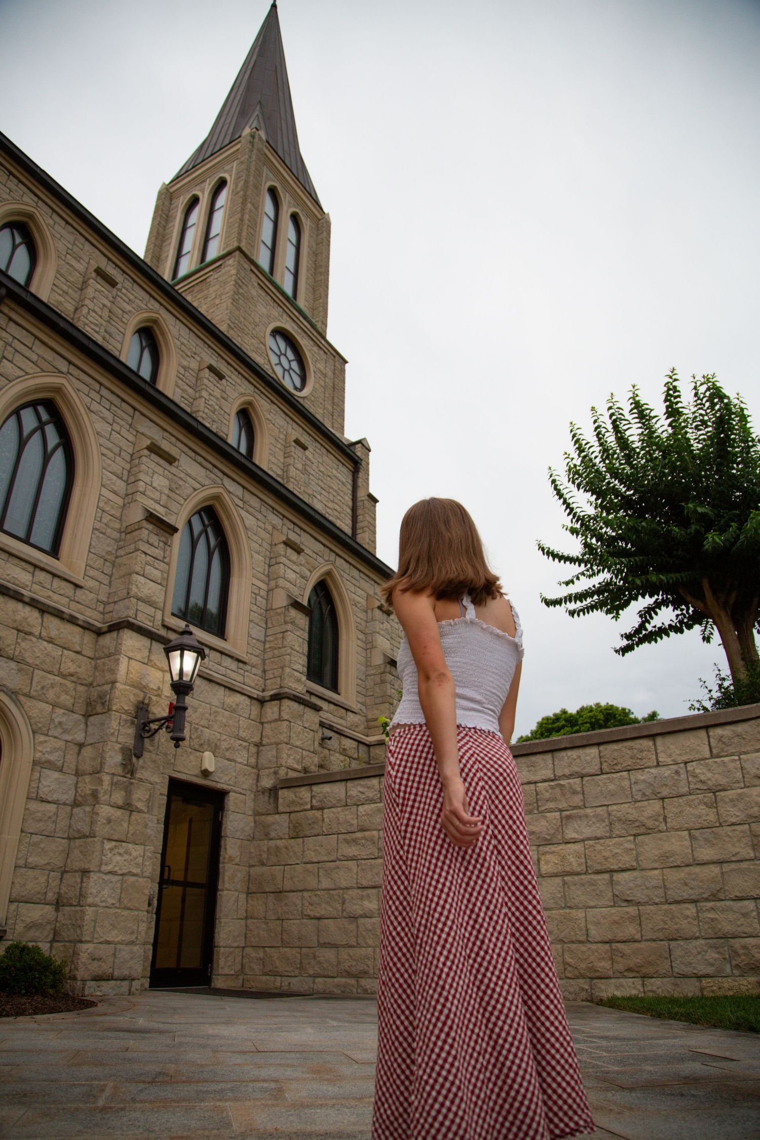 Young woman in white top and plaid skirt standing before gothic stone church.