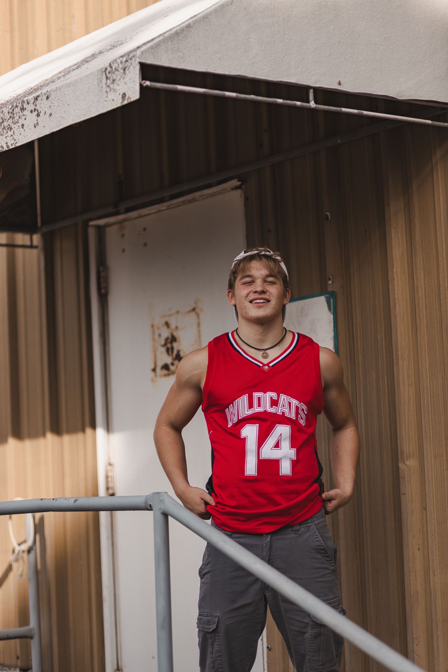 Smiling teen in Wildcats 14 jersey standing on an outdoor staircase railing.