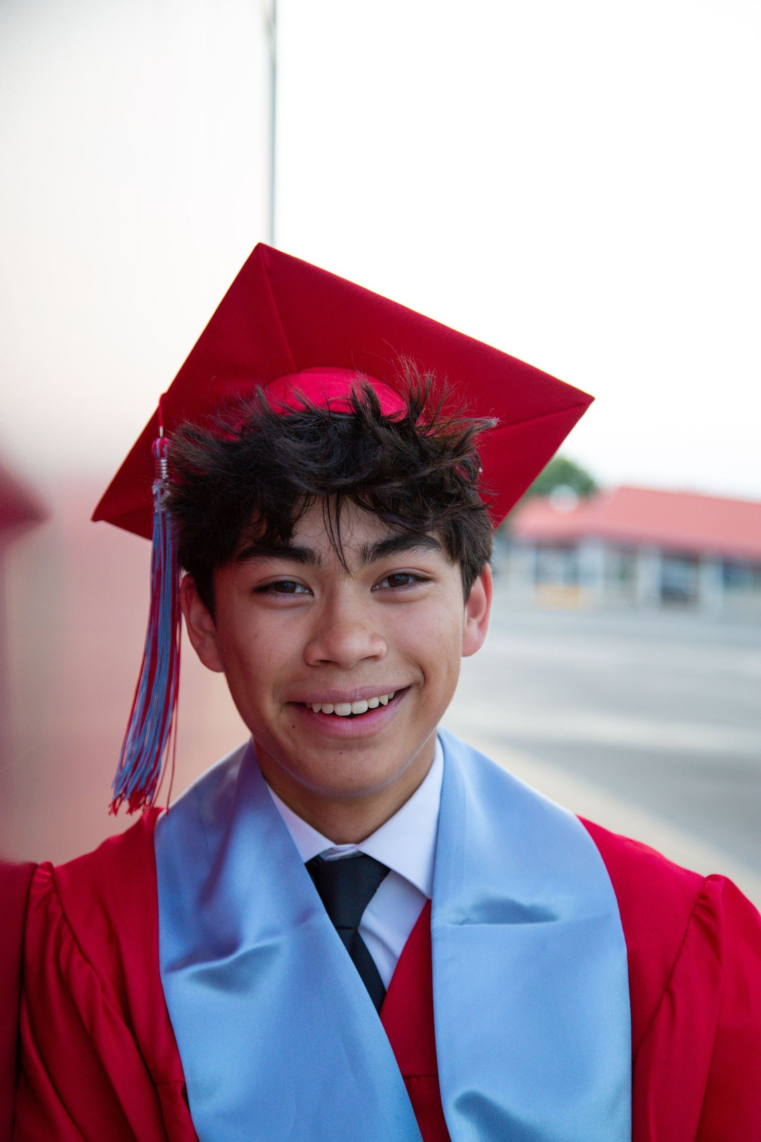 Smiling young male graduate in red cap and gown posing outdoors for graduation photos.