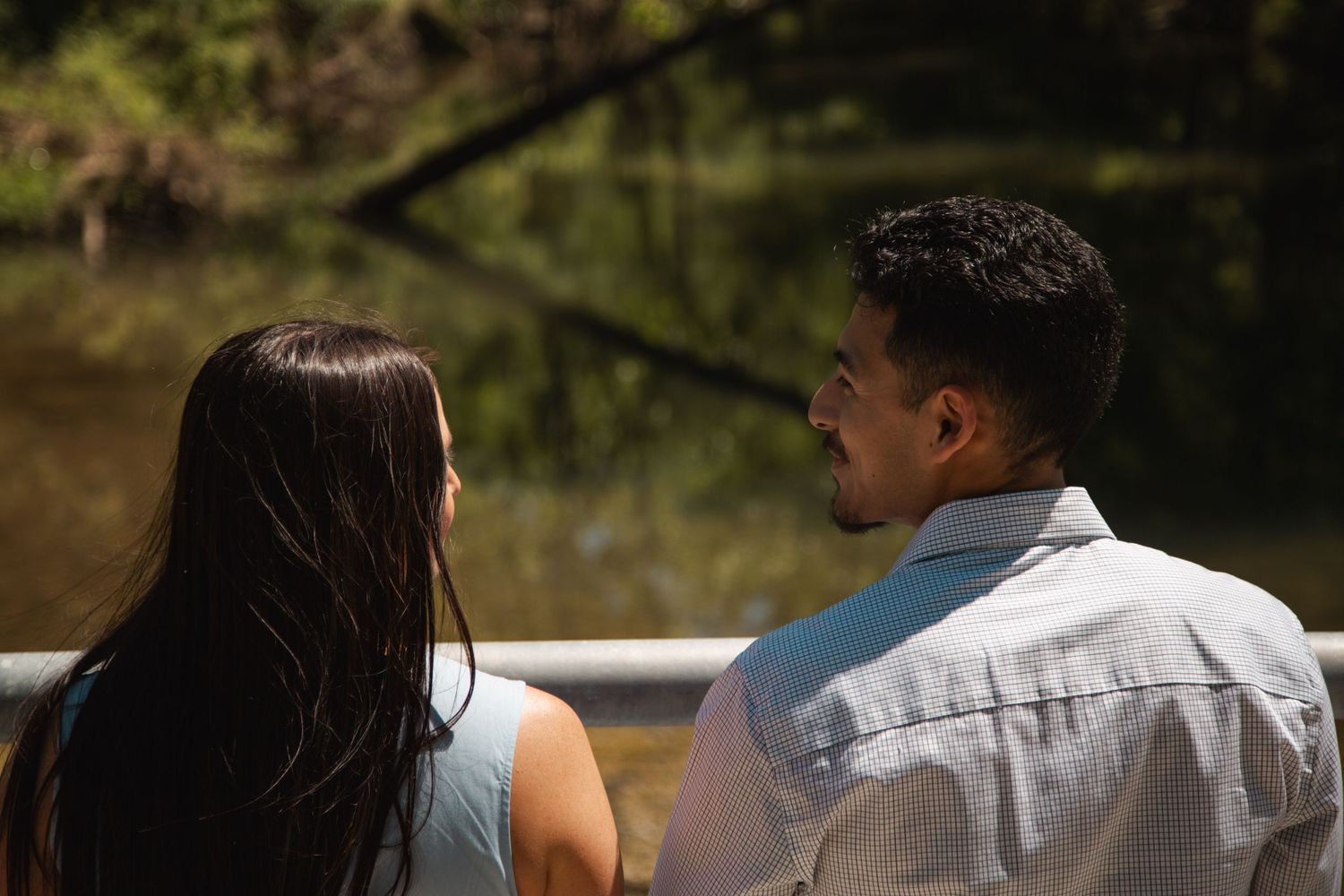 Couple viewed from behind looking at a serene pond surrounded by trees.