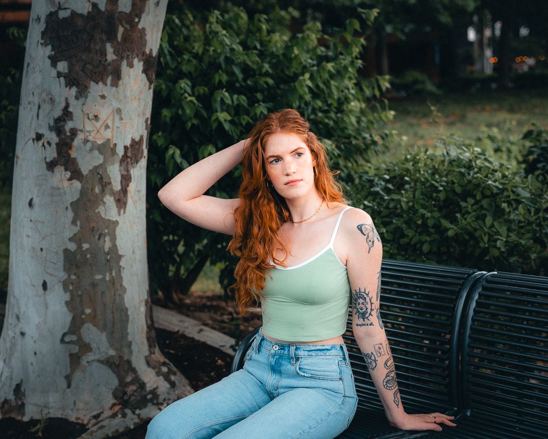 Outdoor portrait of a red-haired woman seated beside a tree