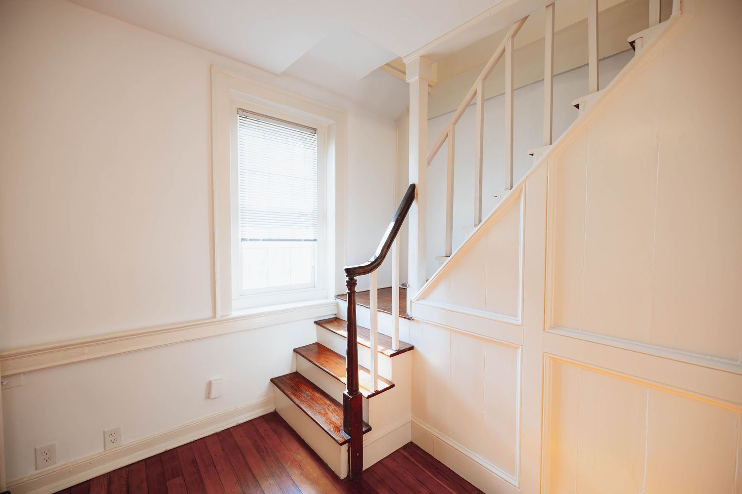Sunlit dining room with hardwood floors, staircase, and chandelier