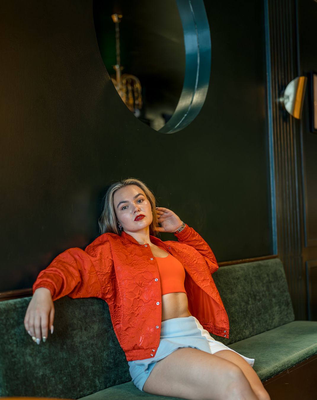 Portrait of a woman in a red jacket seated against a dark wall