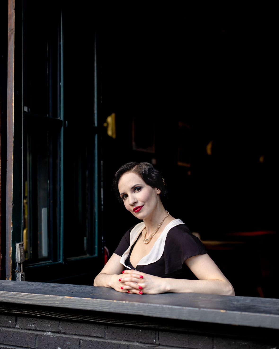 Portrait of a woman in vintage-inspired clothing looking through a dark window