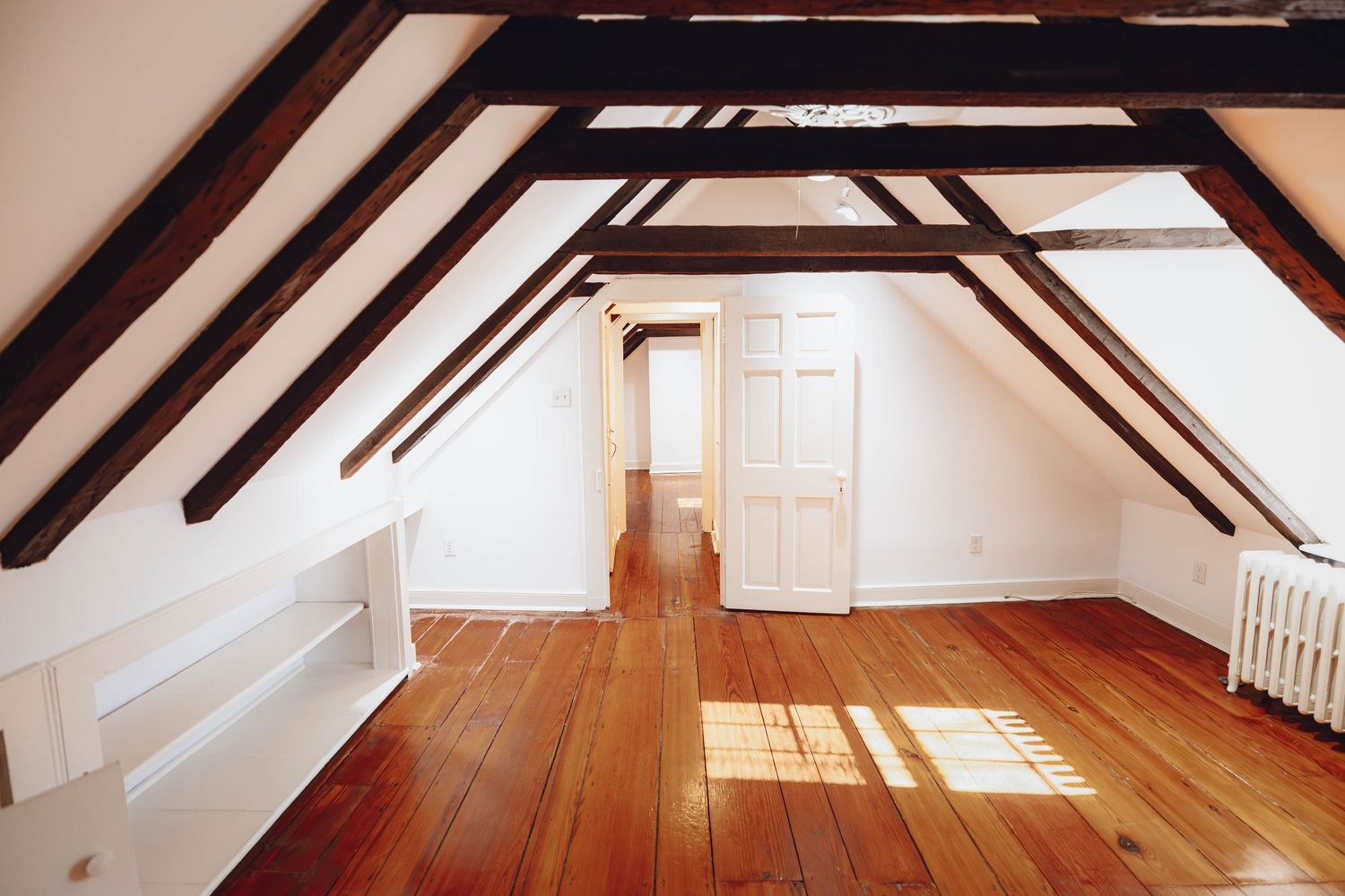 Attic bedroom with exposed dark wood beams and hardwood floors