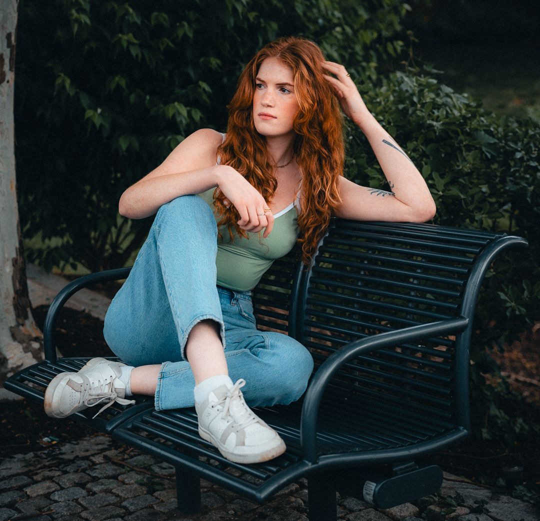 Outdoor portrait of a red-haired woman seated beside a tree