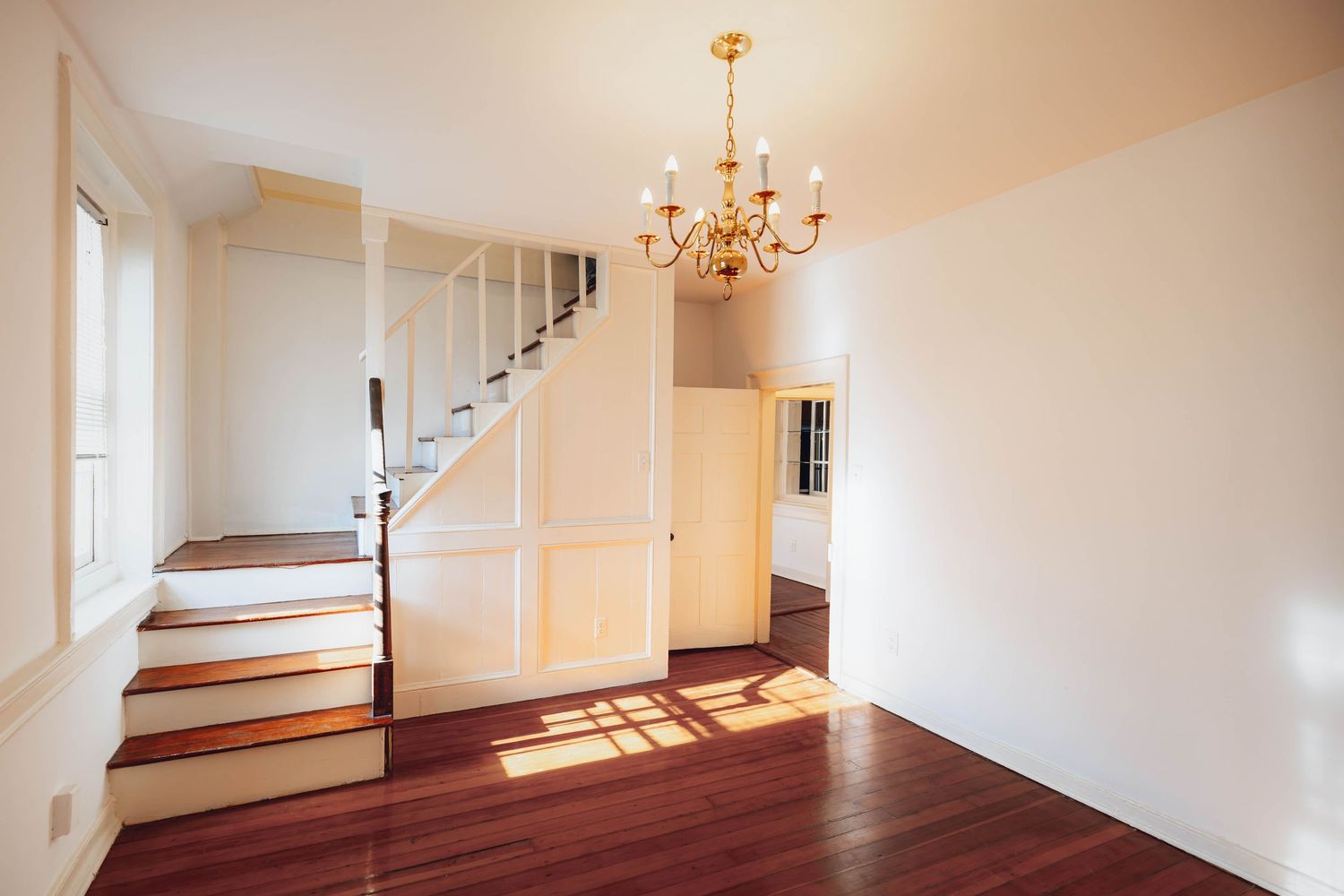 Sunlit dining room with hardwood floors, staircase, and chandelier