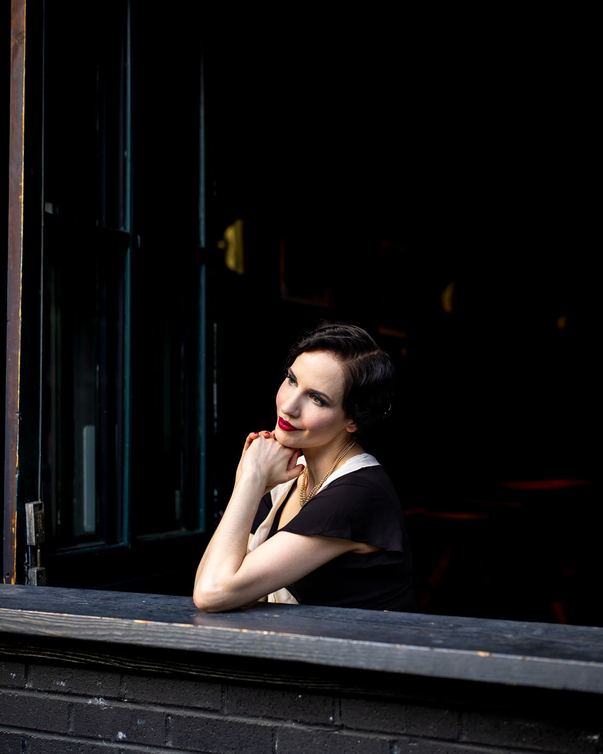 Portrait of a woman in vintage-inspired clothing looking through a dark window