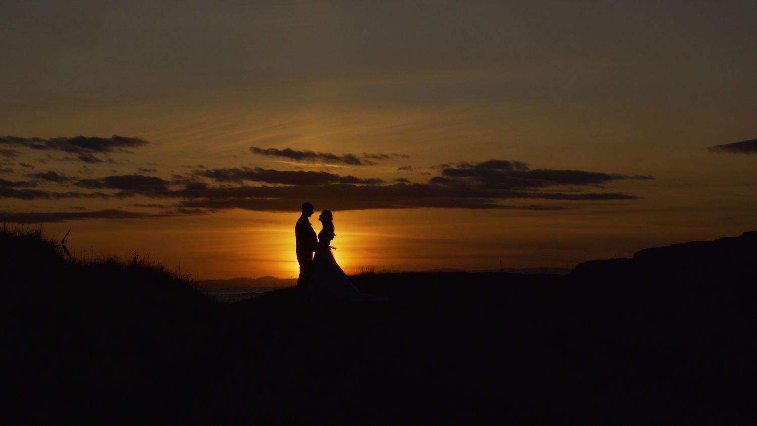Romantic silhouette of a couple embracing against a vibrant golden sunset sky.