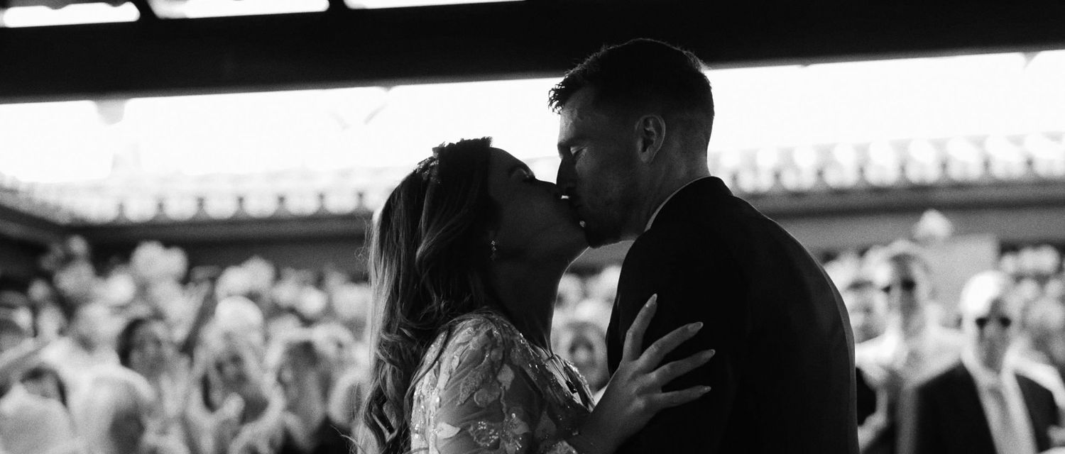Romantic black and white photo of newlyweds sharing first kiss on wedding dance floor.