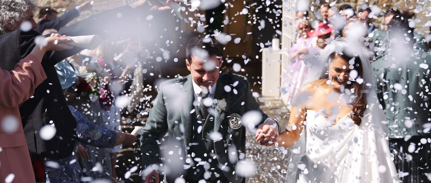 Bride and groom celebrating with confetti shower outside a church on their wedding day.