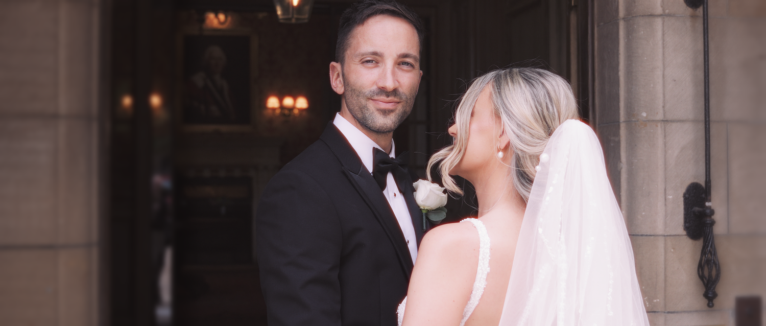 Elegant wedding couple posing at a grand venue entrance, bride in white veil.