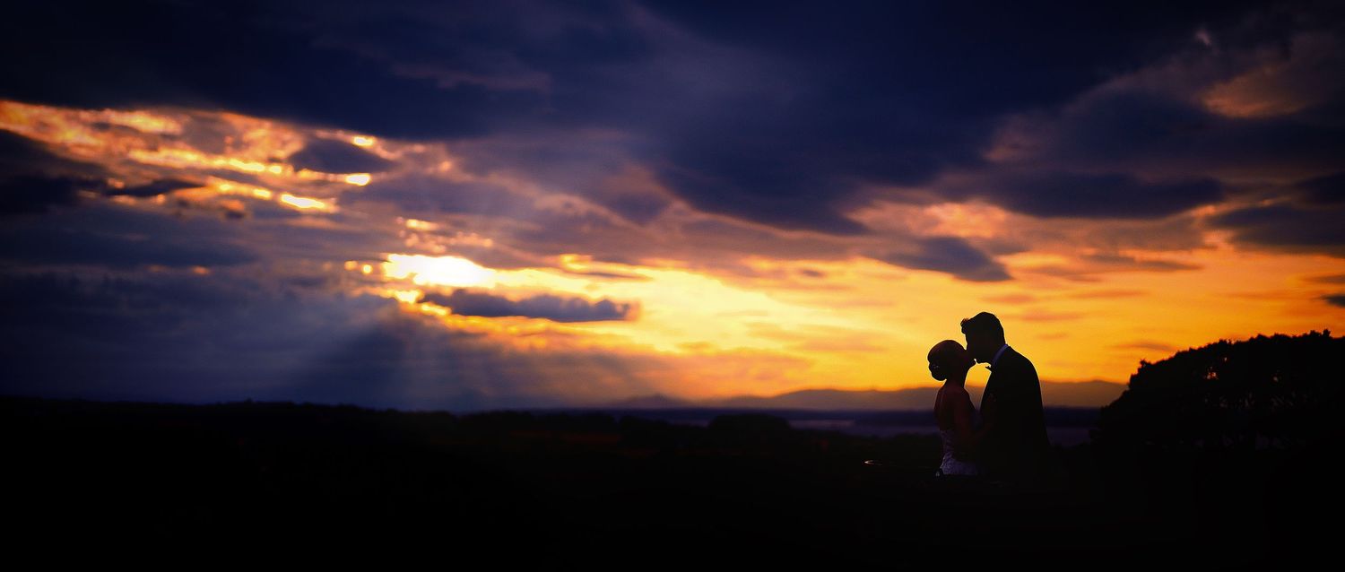 Silhouette of bride and groom sharing a kiss against a stunning golden sunset sky.