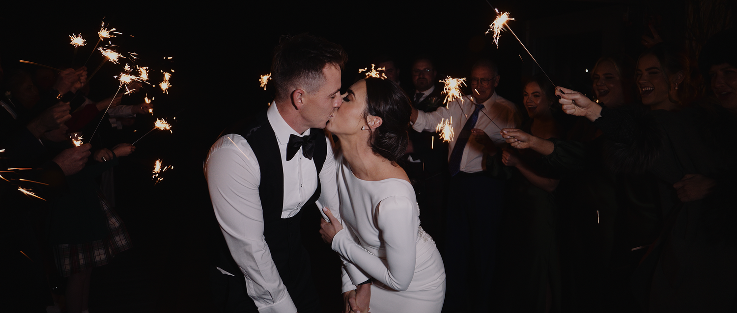 Bride and groom sharing a kiss surrounded by sparklers in a romantic nighttime wedding celebration.