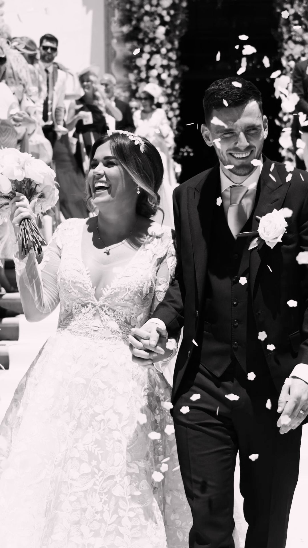 A joyful bride and groom walk through a shower of confetti in a classic black and white wedding photo.