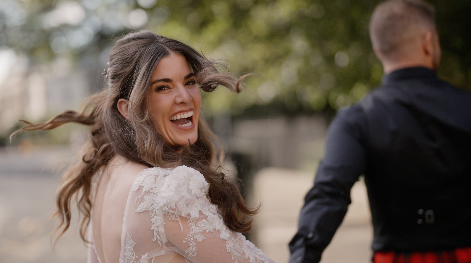Radiant bride in lace wedding dress laughing joyfully outdoors with hair flowing in the wind.