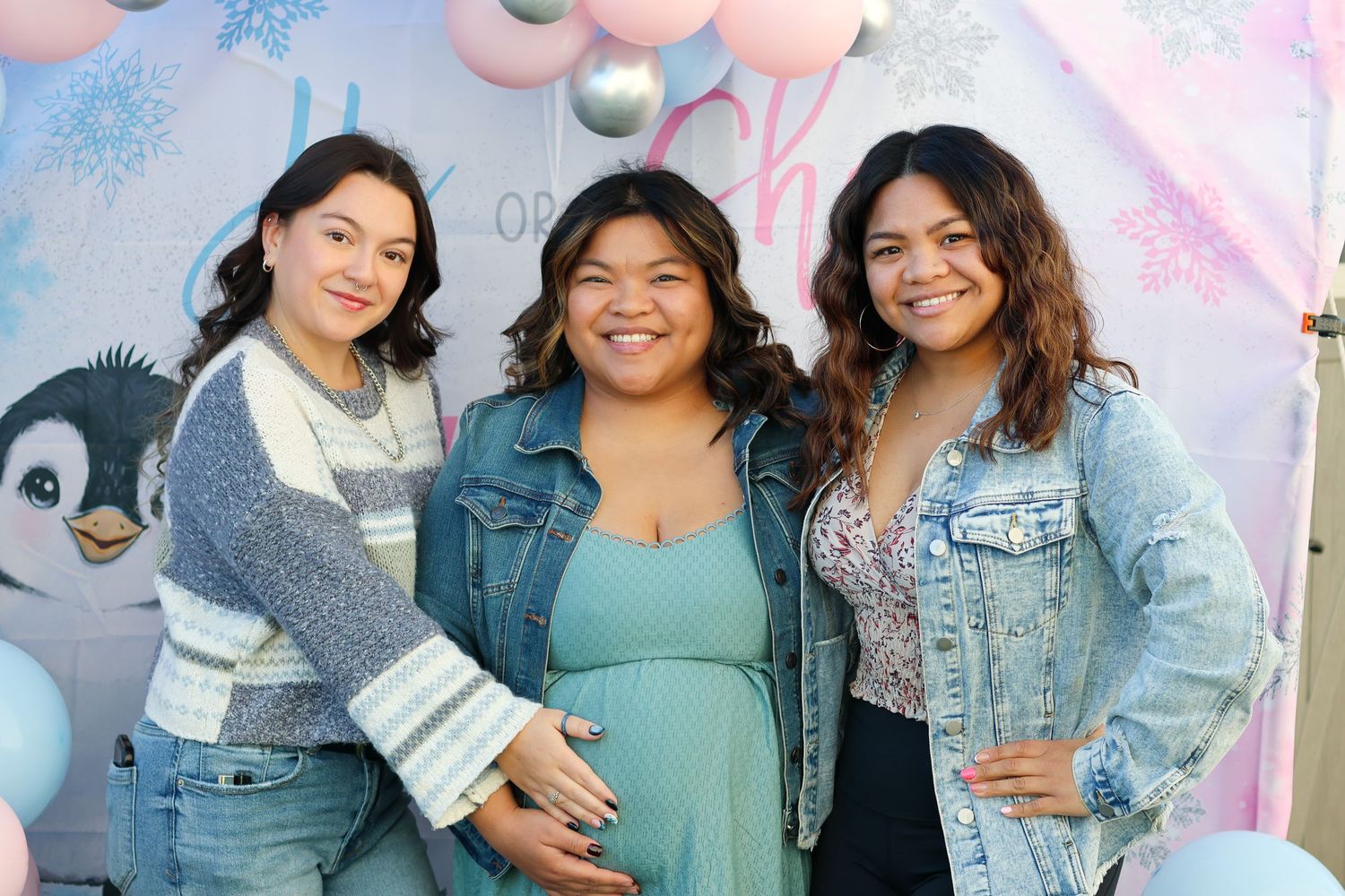 Three friends in denim jackets pose together against a pastel background with festive decorations.