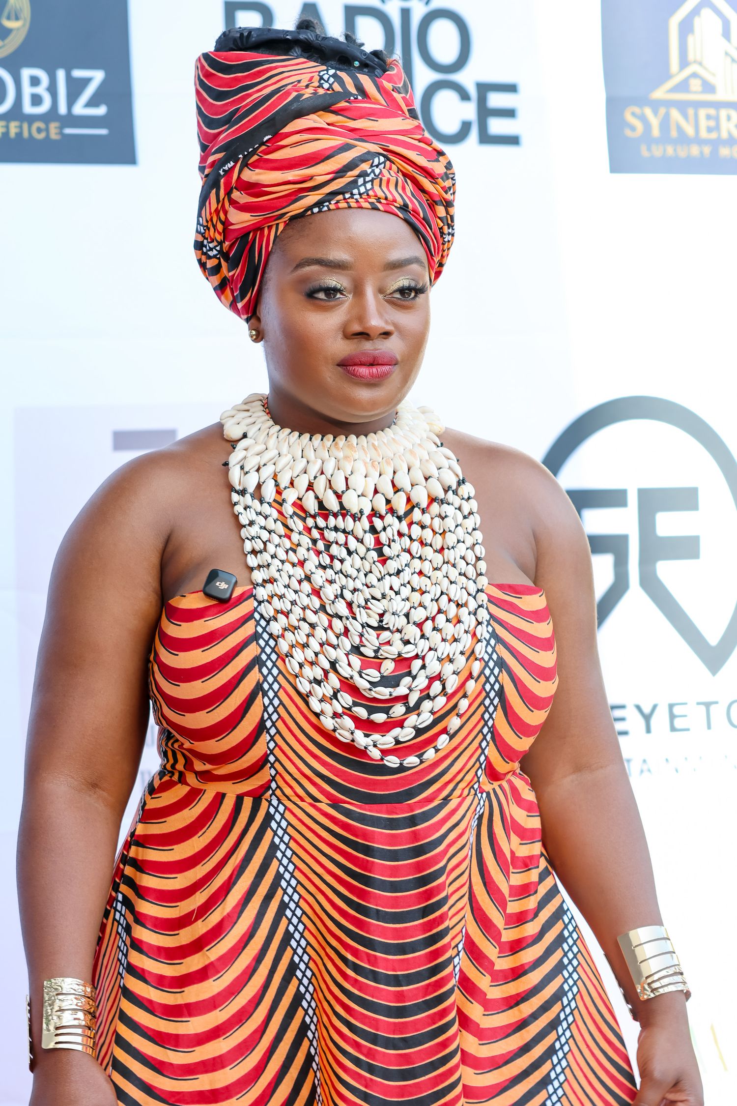 Three people wearing matching red and black traditional African attire with beaded necklaces and head wraps pose together.