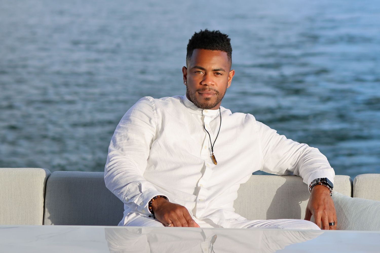 Person in white formal attire relaxes on waterfront furniture during a photo session.