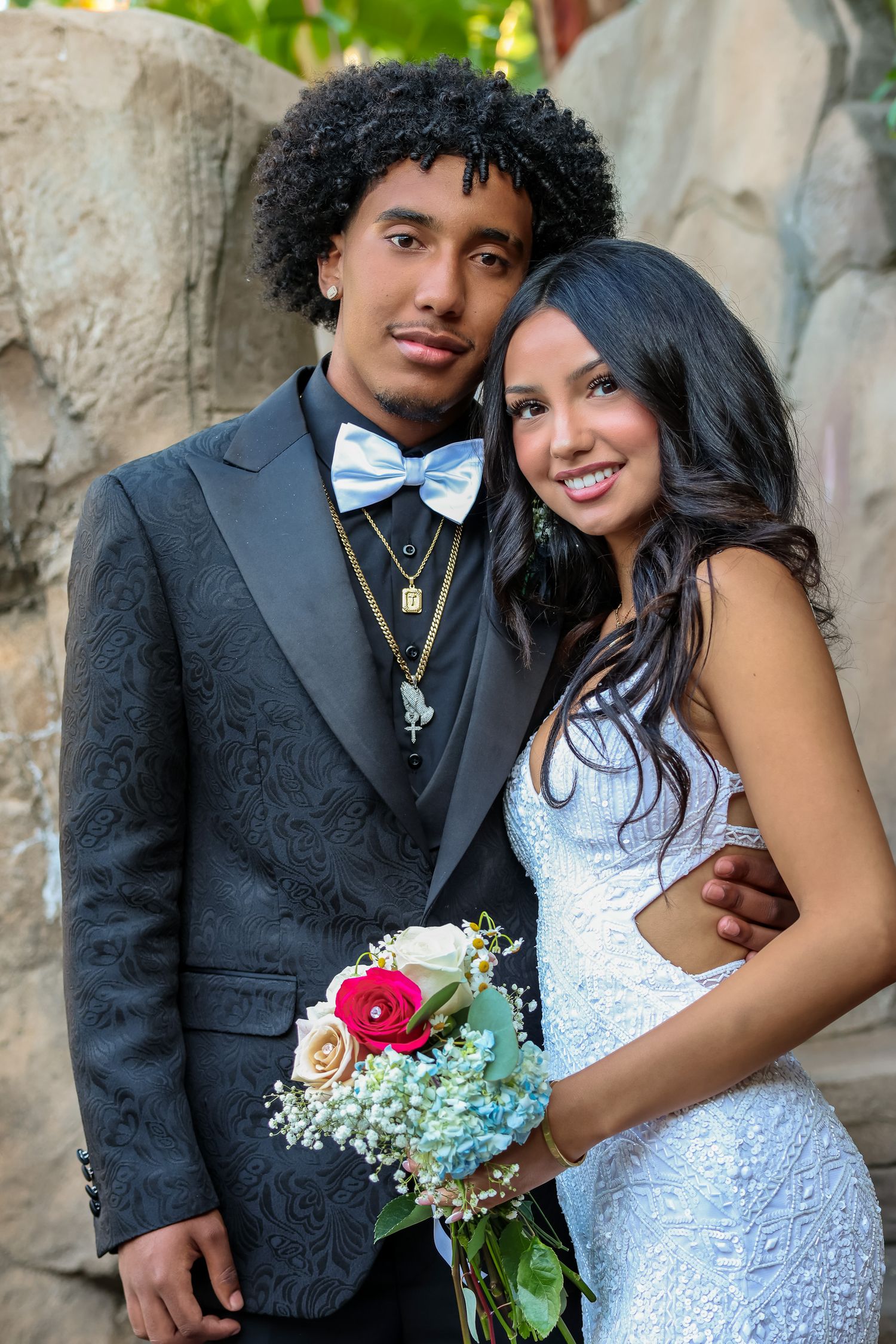 A romantic wedding photo series showing a couple in formal attire posing against a stone wall with floral bouquet details.