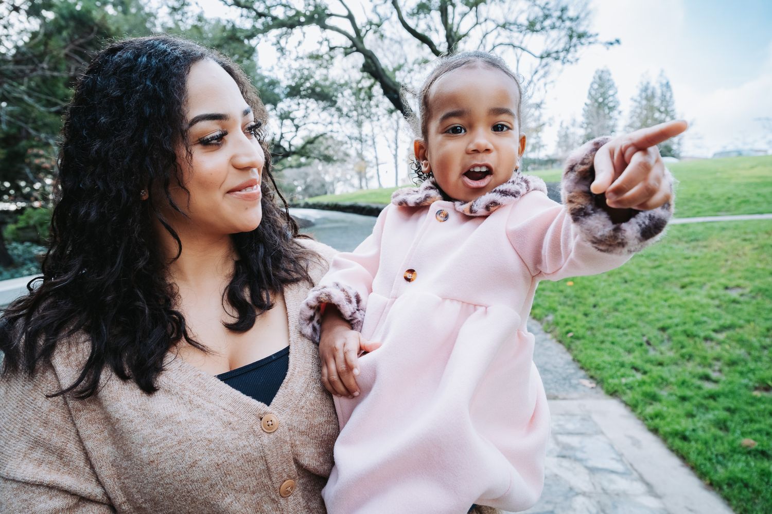 A joyful outdoor photoshoot with people and a small dog in pink outfits on a grassy hill.