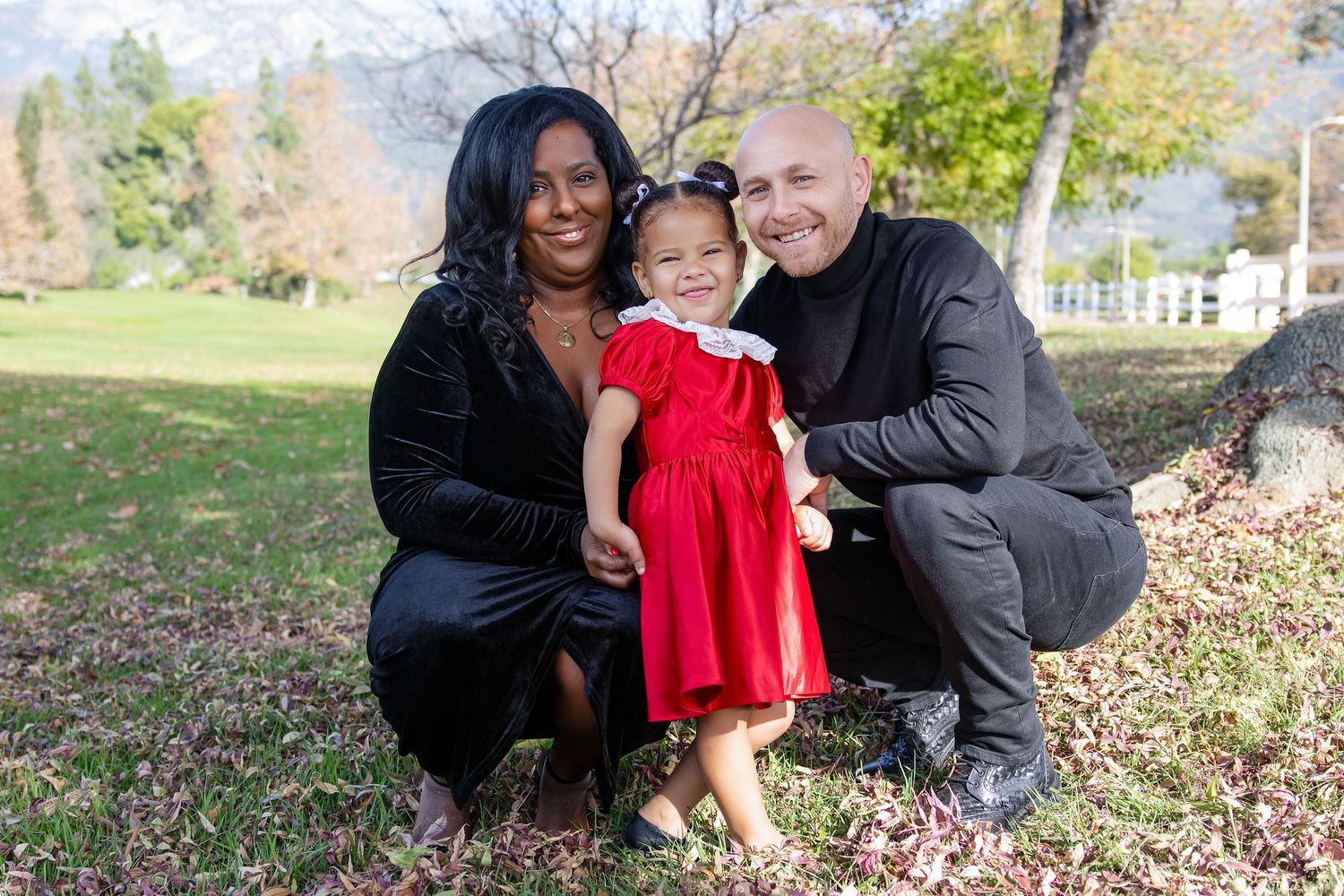 A family enjoys a fun autumn photoshoot together outdoors among fallen leaves in a park setting.