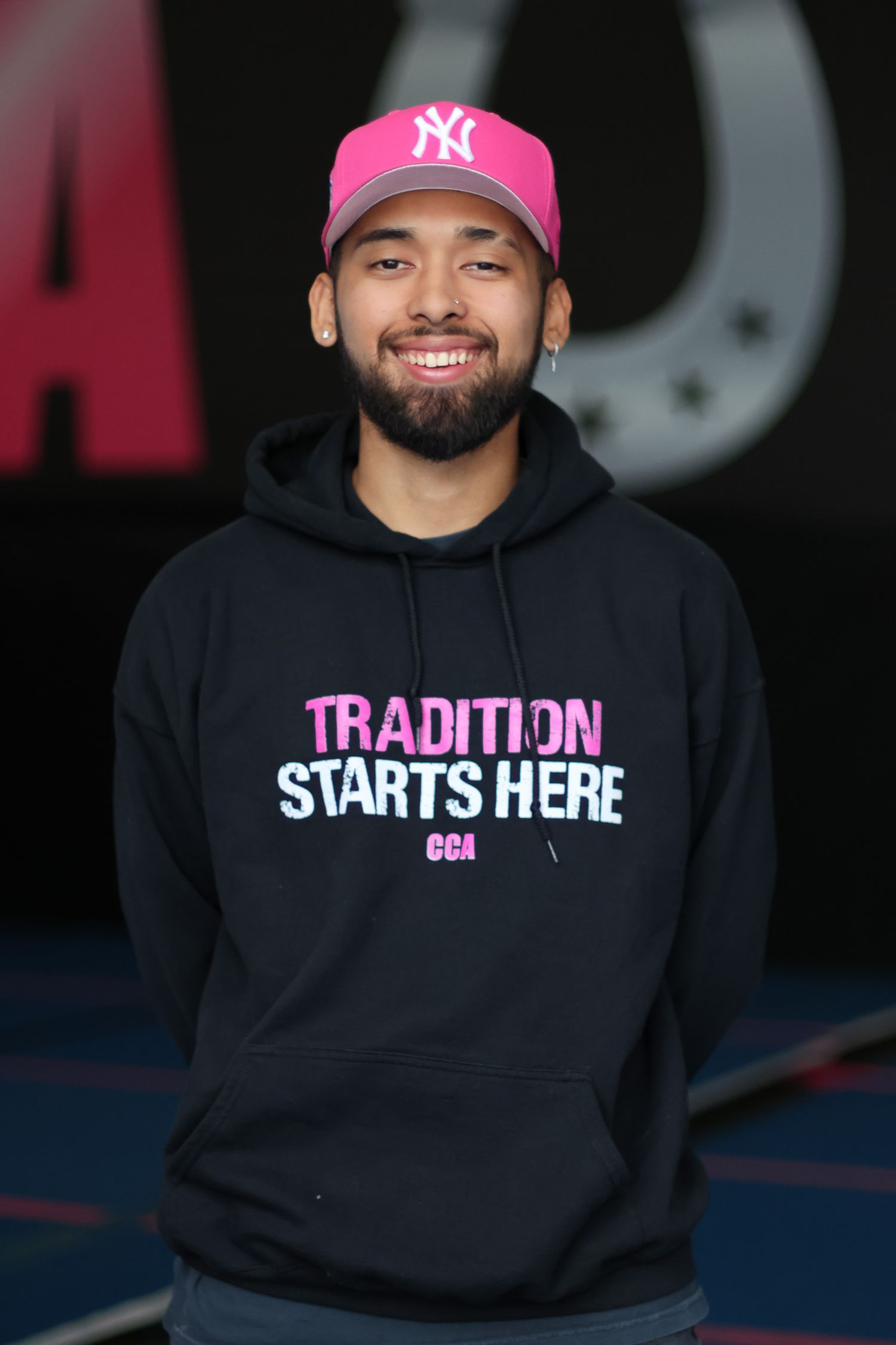 Person wearing black hoodie with 'Tradition Starts Here' text and baseball cap.