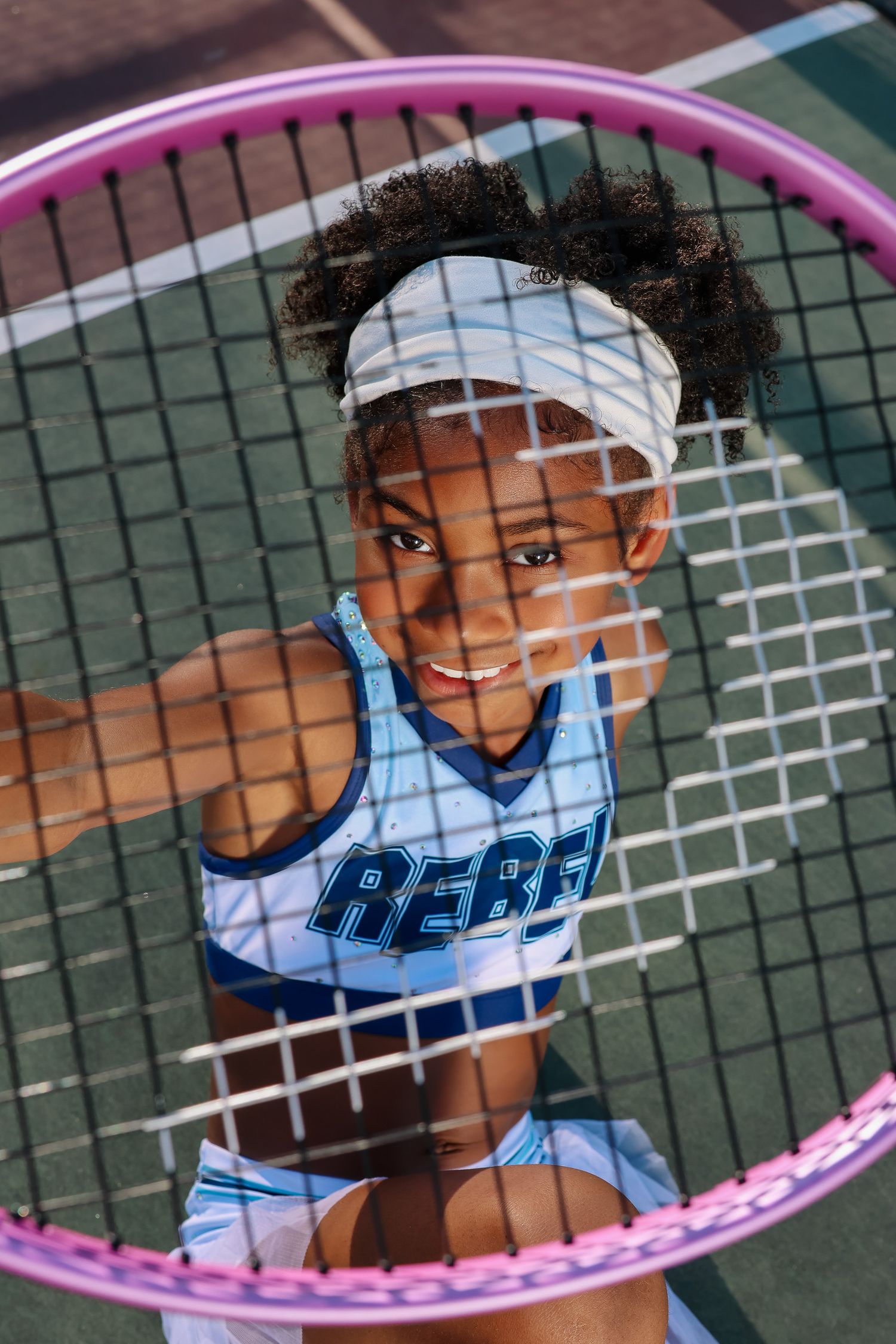 Young athlete viewed through pink tennis racket frames on tennis court.