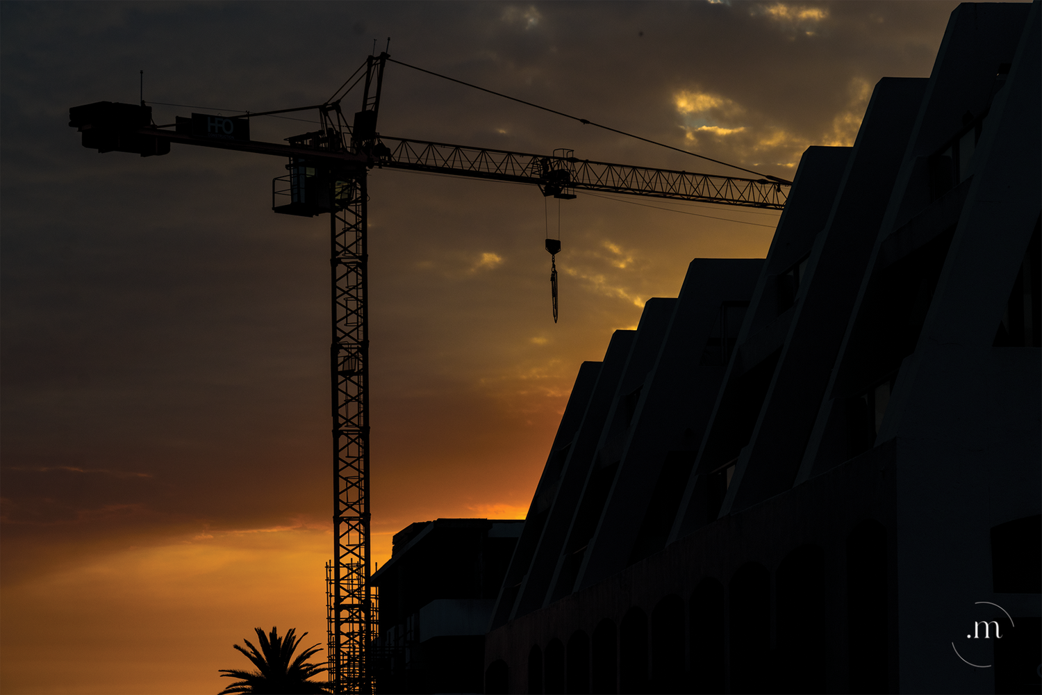 Construction crane silhouetted against a sunset sky