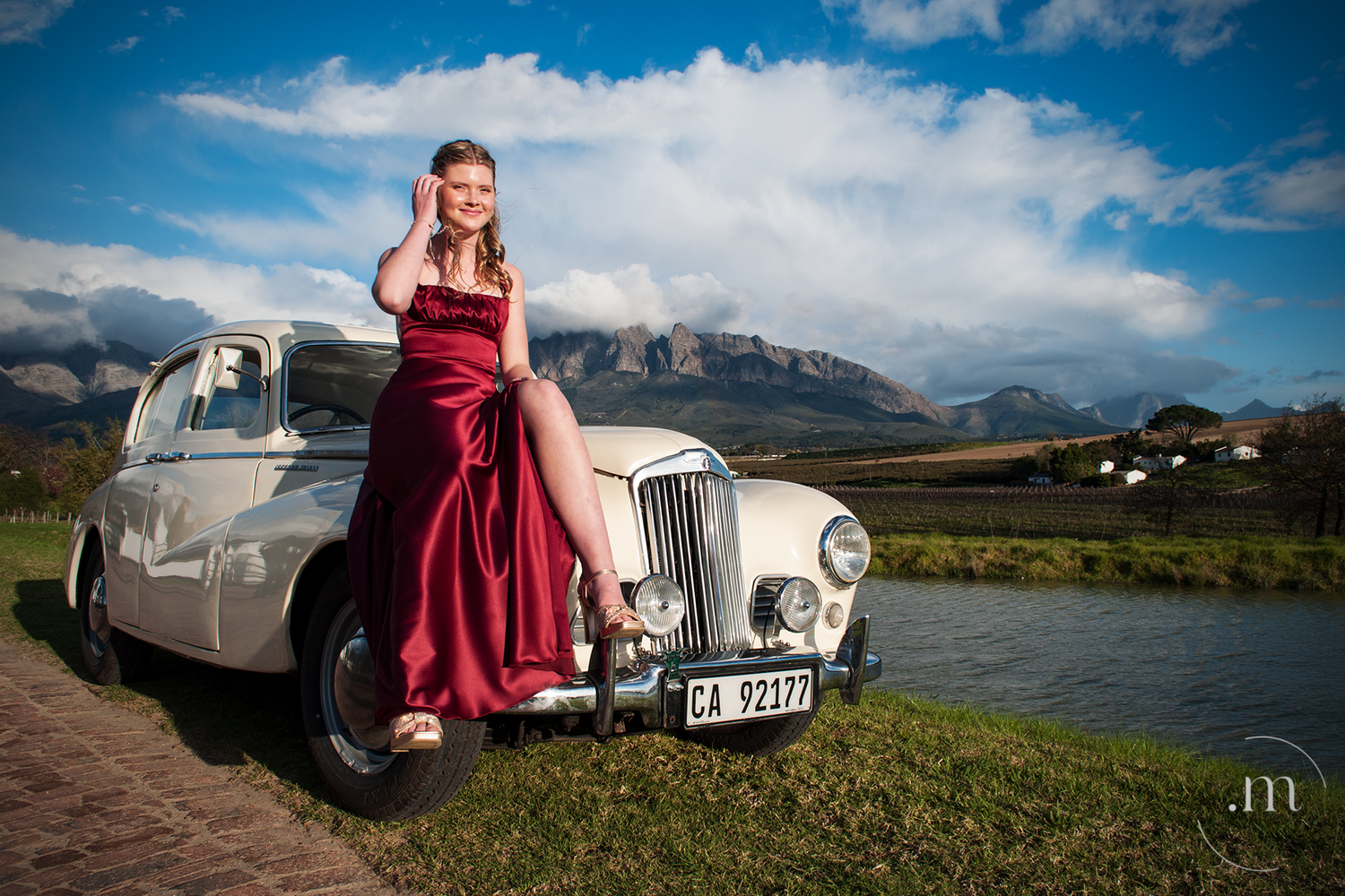 Red dress beside a vintage white car with mountains in the background