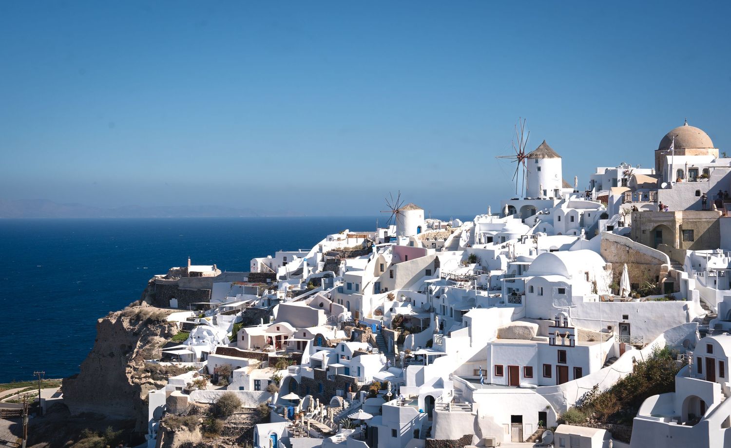 Traditional white windmills and buildings perched on Santorini's cliffs overlooking the Aegean Sea.