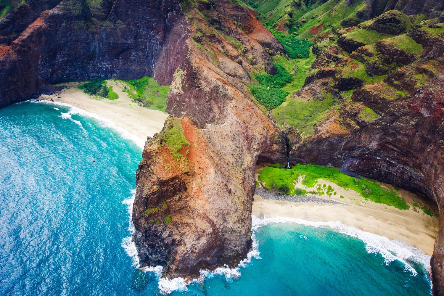 Aerial view of Na Pali Coast's emerald cliffs and pristine beaches along turquoise waters.